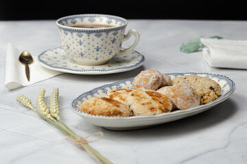Close up shot of cup of red tea with plate full of wheat and oatmeal cookies on marble top and small black background.