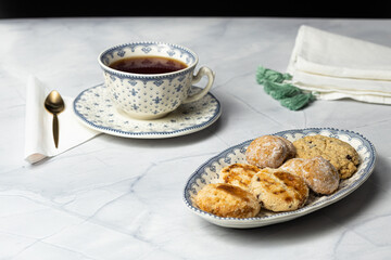 Close up shot of cup of red tea with plate full of wheat and oatmeal cookies on marble top and small black background.
