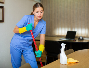 Young woman from a cleaning company conducts a wet cleaning of the office with a rag and detergent