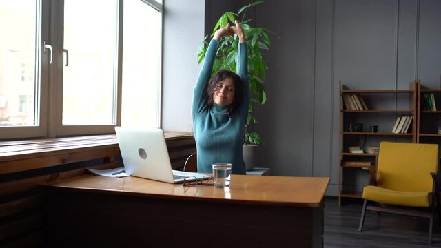 Smiling woman satisfied stretching hands after work done. Happy businesswoman or student relaxing at workplace sit leaning back with feet on desk enjoy rest from online or remote occupation at laptop