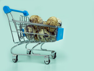 Easter.Online trade.Shopping over the Internet.Mini supermarket cart with quail eggs on blue...