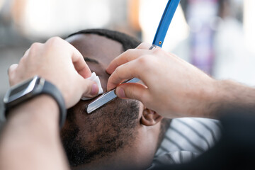 Haircut beard at the barbershop. African American man in a barbershop studio. Professional hairdresser cutting his beard