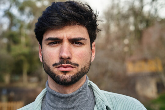 Serious bearded male standing in park