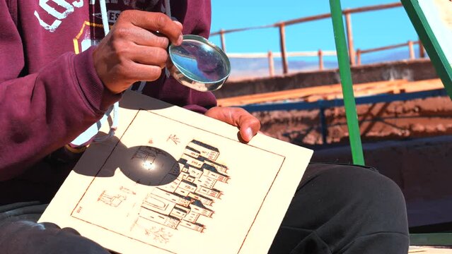 Young man sitting and looking at drawing on paper through magnifying glass at desert
