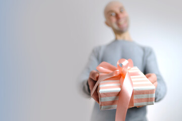 close-up of white, pink gift, box with satin ribbon in hands of young man, gives surprise to loved one, girlfriend, mom, concept of mother's, Valentine's day, birthday, christmas gift
