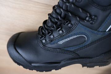 close-up of one new black work boot with lacing made of leather with reinforced cape, high top on wooden floor, concept of special protective professional shoes, professional work safety