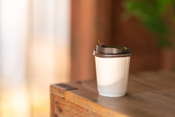 Closeup of disposable take away paper cup of hot coffee on wooden table.