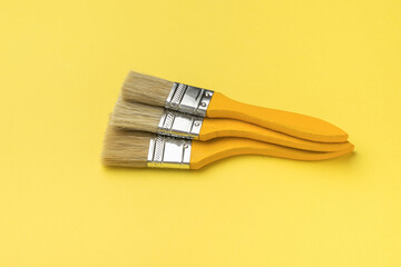 Three brushes with yellow wooden handles on a yellow background.