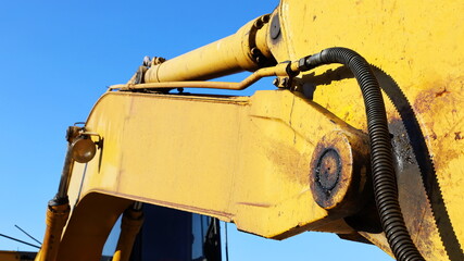 Excavator arm with hoses and hydraulic cylinders. Hydraulic system of old yellow backhoe in white...