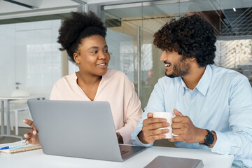 Fototapeta premium African American and Indian friendly colleagues talking in office at laptop