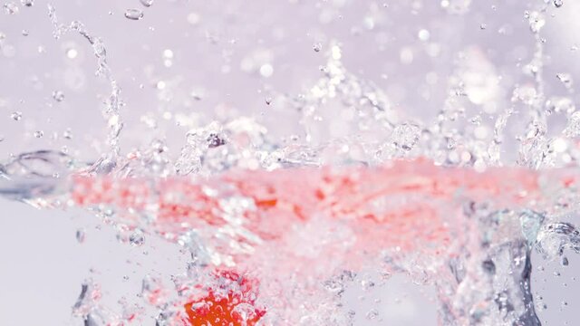 SLOW MOTION TIME WARP, CLOSE UP, HALF UNDERWATER: Vibrant ripe cherry tomatoes splash into the refreshingly cold water. Detailed close up shot of tomatoes falling into a container full of glassy water