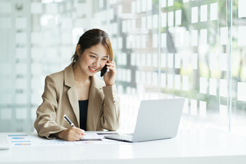 Portrait of young asian business woman talk on smartphone write notebook laptop in home office. Beautiful girl at desk computer take home order. Startup business asia woman online sme telemarketing.