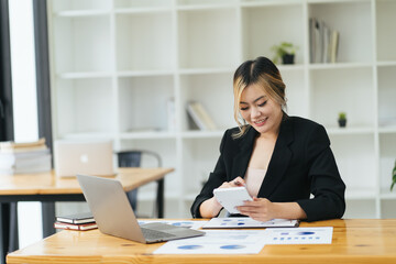 Young Asian woman entrepreneur/ Business owner using a smartphone and working with computer at home