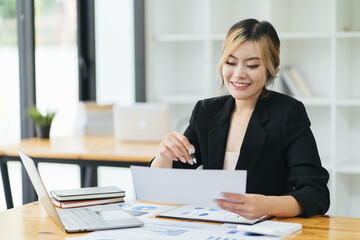 Pretty and charming asian businesswoman sitting happily smiling with laptop computer in the office.