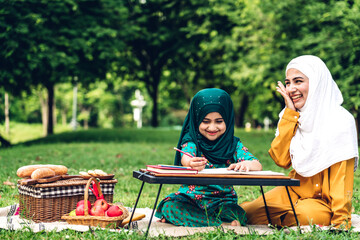 Portrait happy love asian muslim family mother teach little daughter muslim girl learn and study.Mom and muslim girl writing with book and pencil making lessons in green park.Education