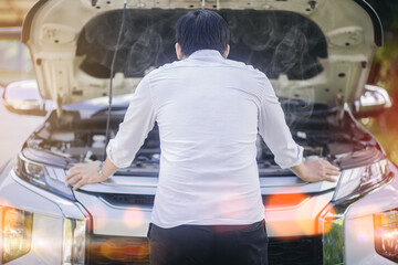 A broken down car, engine open and smoking, serious driver looking at the engine and do nothing....