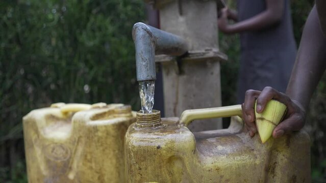 Close up shot of a water fountain filling dirty water cans in African village. African drought concept 4K.