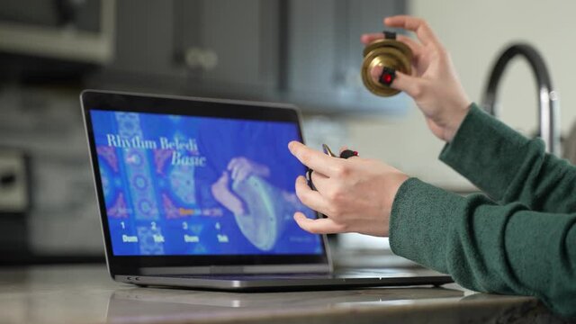 Woman takes remote lesson to learn finger cymbals online on a laptop. Remote learning concept.