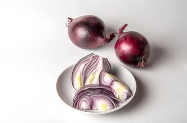 Red onion, whole, unpeeled and peeled, sliced on a plate on a white background.