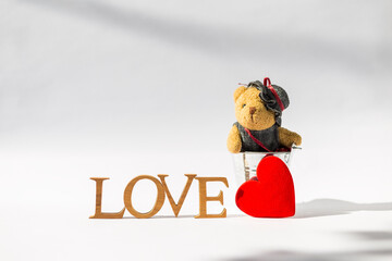 Little cute teddy bear in metal bucket and red heart with love wooden font with space on white background, morning day light, valentine concept, love and romance background