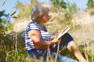 Naklejka na ściany i meble Blurred Woman relaxing outdoors and reading book