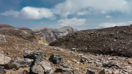 The top of an active volcano. Rocky soil is visible, the layered structure of the crater. Blue sky with picturesque clouds. Kamchatka. Gorely Volcano