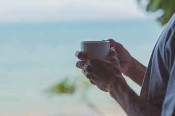 Male hands holding coffee cup looking out to sea view in front of bedroom and think of something in a relaxed atmosphere, Business planning with work from home or vacation relaxation concept.