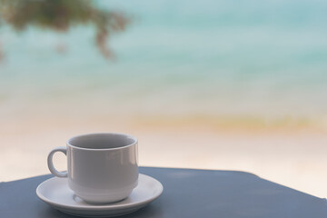 White coffee cup on gray table There is space on the side for design or product placement. beautiful sea and nature blur background, Relaxing and vacation concept, Samui Thailand beach.