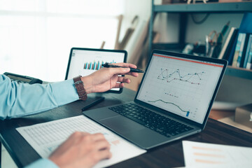 Business man hold stylus pen and pointing to laptop at office  with document report, graph, financial report on screen.