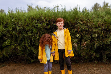 Fototapeta premium Redhead siblings in yellow raincoats in park