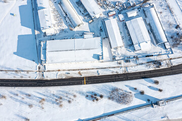 Naklejka na ściany i meble aerial top view of snow-covered storage buildings and warehouses in an industrial district at sunny winter day