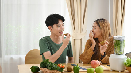 Happy young couple enjoying preparing green detox vegetable smoothie. Healthy lifestyle concept.