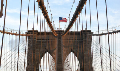 Flag of America winding on top of Brooklyn Bridge from New York during sunset.