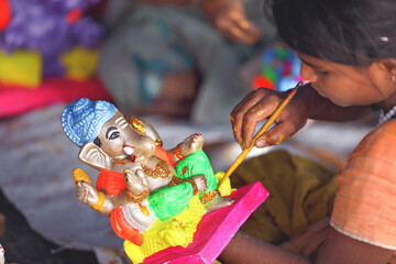 Indian little girl painting the god doll for festival