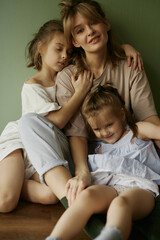 Mother and two funny daughters laughing and playing together. Sisters. Friendship. Family relationships. Green wall. Natural light. Love and happiness. Emotional and cute girls . Casual home clothes. 