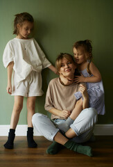 Mother and two funny daughters laughing and playing together. Sisters. Friendship. Family relationships. Green wall. Natural light. Love and happiness. Emotional and cute girls . Casual home clothes. 