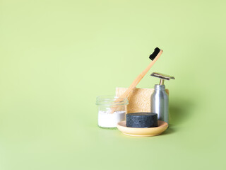 The bamboo toothbrush with toothpowder and the steel multiple-use razor in the bottle, one natural round soap and the natural wash gourd against the green background. Zero waste bathing concept.