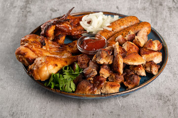 Assorted grilled meat in a plate on the table. Fried chicken legs and wings, sausages, shish kebab, pickled onions and tomato sauce. Horizontal orientation, copy space, no people