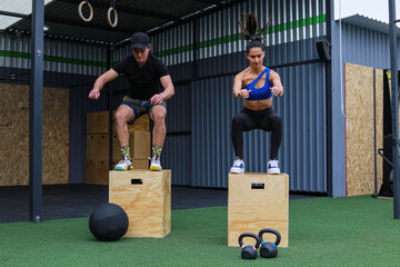 A man and a woman doing box jumps inside a crossfit GYM