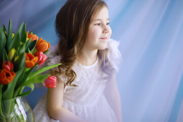 Beautiful girl in white dresses with a magnificent bouquet of the first tulips. International Women's Day. Girl with tulips.