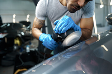 Fototapeta na wymiar Car detailing. Male hands with orbital polisher in auto repair shop
