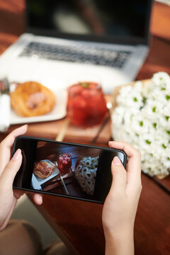 Close-up image of woman taking photos of refreshing drink and sweet pastry she ordered in cafe