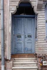 Blue wooden door in wooden house with drainpipe. Stone staircase. Vertical photo.