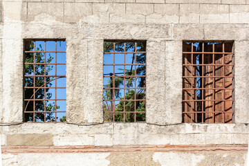 Three windows with bars in block wall. One window has shutters. Horizontal photo.