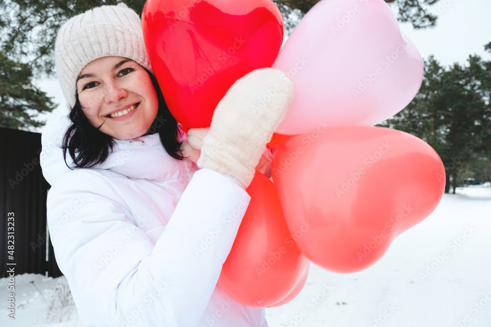 Wall mural Happy woman with heart-shaped balloons outdoor in winter with snow. Valentine's Day, love and infatuation, a gift from a boyfriend, a declaration of love, lifestyle