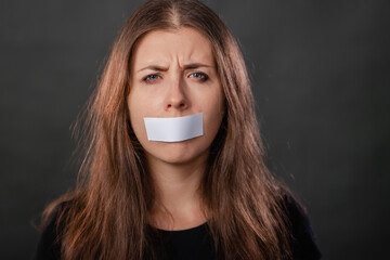 Close-up portrait of a young woman with duct tape sealed in her mouth, restriction of freedom of...