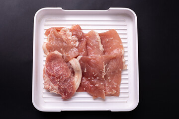 Top view of raw sliced pork marinated with white sesame on white tray isolated on black background. menu for buffet food. meat prepared for yakiniku or sukiyaki.