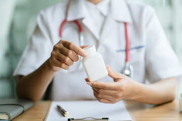A doctor or pharmacist sits at a desk, holds or shows a bottle of medicine in his hand and writes a prescription explaining its properties. Concept of medical treatment, pharmacy or health insurance