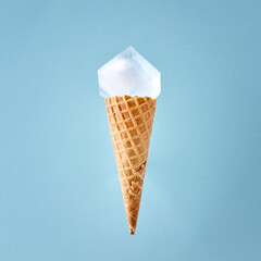 Ice cream waffle cone with a big ice cube on blue background. Minimal cold summer food concept.