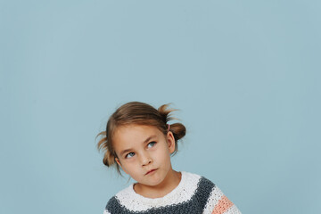 Looking up tight-lipped little girl in striped sweater, hair in buns over blue